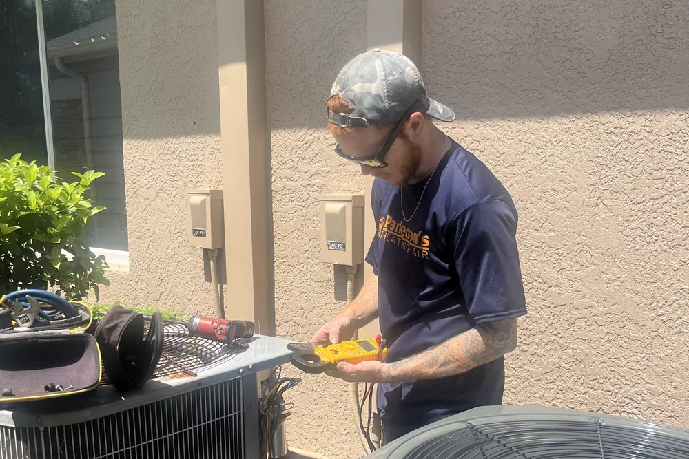 Parkersons Heating and Air technician testing an outdoor condenser unit with a digital multimeter